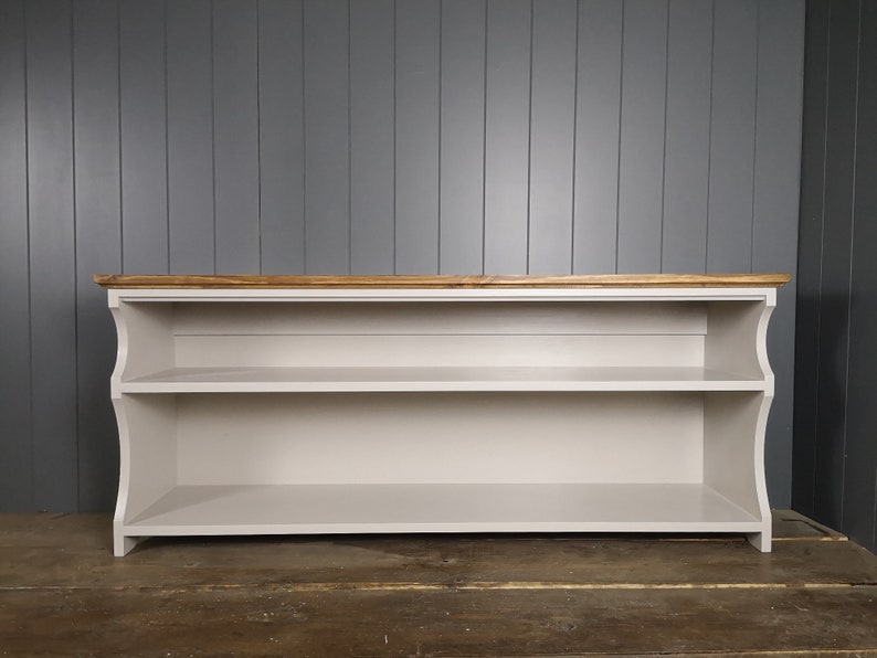 May include: A white wooden shelf unit with two shelves and a natural wood top. The shelf unit has a curved front and is standing on a wooden floor.