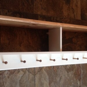 May include: White wooden wall shelf with a natural wood top and six wooden hooks. The shelf has two compartments.