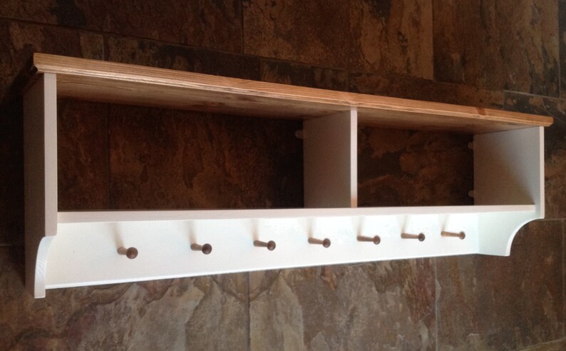 May include: White wooden wall shelf with a natural wood top and six wooden hooks. The shelf has two compartments.