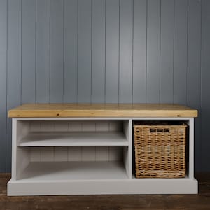 May include: A gray wooden bench with a light wood top and a wicker basket in the right compartment. The bench has two shelves for storage.