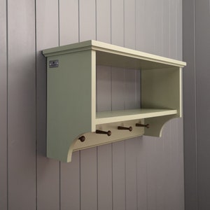 A painted coat rack with a storage or display shelf and wooden pegs to hang coats.