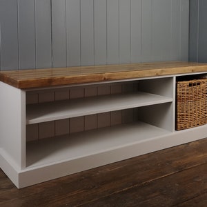 May include: A white painted wooden bench with a natural wood top and two shelves. The bench has a storage compartment on the right side with a woven basket inside.