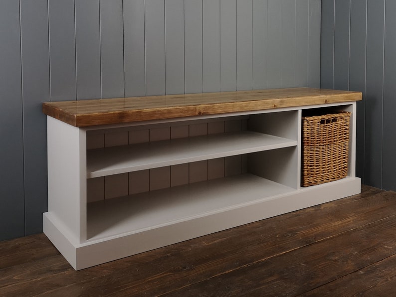 May include: A white painted wooden bench with a natural wood top and two shelves. The bench has a storage compartment on the right side with a woven basket inside.