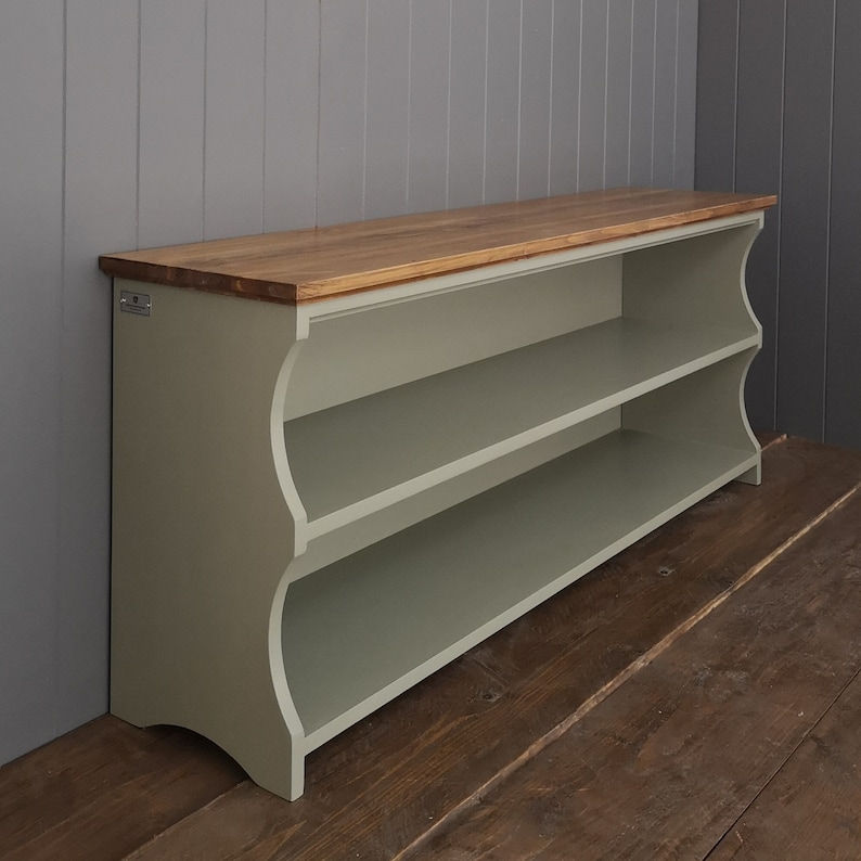 May include: A light green wooden shoe rack with two shelves and a natural wood top. The shoe rack has a curved front and is sitting on a wooden floor.