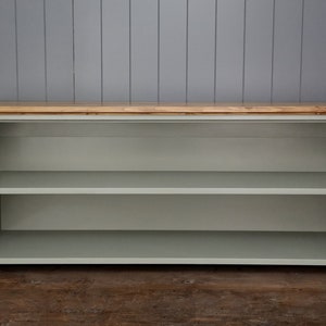 May include: A light green wooden shelf unit with two shelves and a natural wood top. The shelf unit has a curved design on the sides and is freestanding.