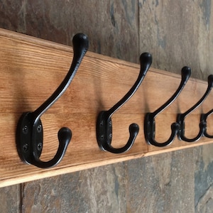 May include: A wooden coat rack with eight black metal hooks. The rack is stained a dark brown colour and has a slightly rounded edge.