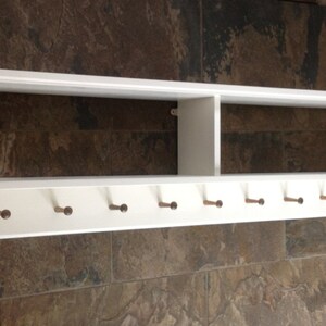 May include: White wooden shelf with a divided top shelf and a row of eight hooks on the bottom. The shelf is mounted on a wall.
