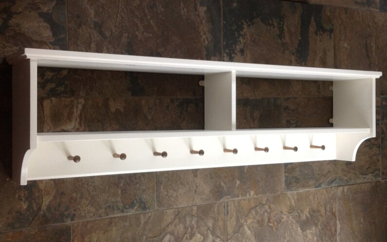 May include: White wooden shelf with a divided top shelf and a row of eight hooks on the bottom. The shelf is mounted on a wall.