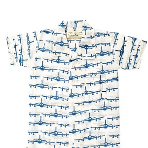 Puede incluir: Mono blanco de manga corta con estampado de avión azul. El mono tiene cuello abotonado y un bolsillo en el lado izquierdo. El texto "night & weekend" está impreso en la etiqueta.