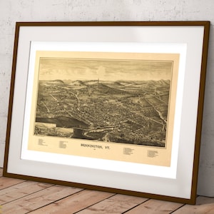May include: A framed sepia-toned bird's-eye view map of Bennington, VT, featuring detailed illustrations of buildings, streets, and surrounding hills. The print includes a legend at the bottom and is encased in a dark brown frame with a white mat.