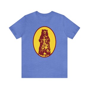 May include: A blue t-shirt with a red bear silhouette inside a yellow circle.