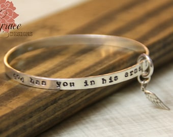 May include: Silver bangle bracelet with the inscription "God has you in his arms" and a small angel wing charm.