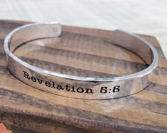 May include: Silver hammered bangle bracelet with the words "Revelation 5:6" engraved on the front.