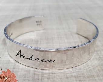 May include: Silver hammered cuff bracelet with the name "Andrea" engraved on it.