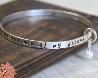 May include: Silver bangle bracelet with a charm and the inscription "Marrying the man of my dreams."