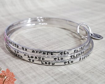 May include: Silver bangle bracelet set with three bands, each engraved with a different inspirational quote: "Strength to accept the things", "Wisdom to change the things", and "To know the difference".