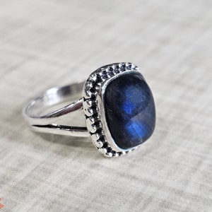 Puede incluir: Un anillo de plata con una piedra preciosa de labradorita azul engastada en un engaste de cuentas.