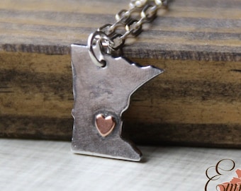 Puede incluir: Un collar de plata con un colgante con forma del estado de Minnesota. El colgante tiene un pequeño corazón de cobre en el centro.
