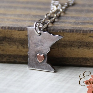 May include: A silver necklace with a pendant shaped like the state of Minnesota. The pendant has a small copper heart in the centre.
