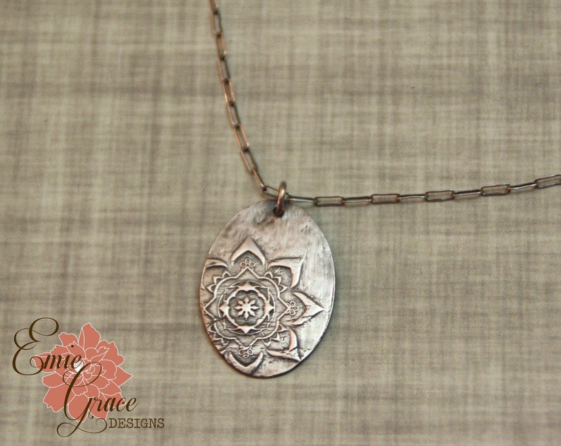 May include: A silver necklace with a round pendant featuring an etched mandala design.