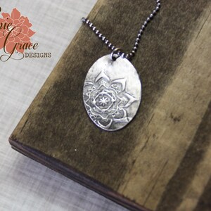 May include: A silver necklace with a round pendant featuring a detailed mandala design. The pendant is hanging on a silver chain.
