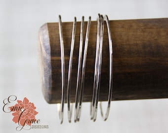 May include: A set of eight silver-toned hammered metal bangles stacked on a wooden surface.