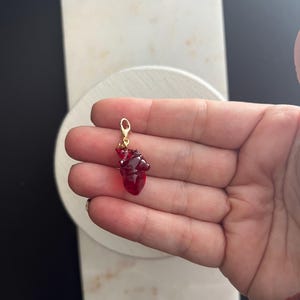 Puede incluir: Un charm de corazón de vidrio rojo con un cierre dorado. El charm es aproximadamente del tamaño de una moneda de 1 euro.