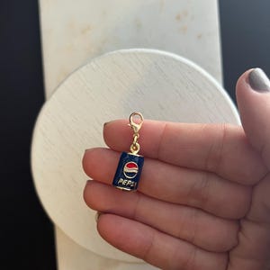 May include: Gold charm shaped like a blue and red Pepsi can with a gold clasp.