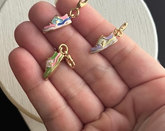 Könnte beinhalten: Drei bunte Sneaker-Anhänger mit goldfarbenen Verschlüssen. Die Anhänger sind in den Farbtönen Rosa, Blau, Grün und Gelb gehalten. Die Sneaker haben ein Sterndesign auf der Seite. Die Anhänger sind klein und detailliert.