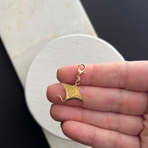 May include: Gold-toned charm featuring a detailed cutout of a manta ray. The charm has a lobster clasp for attaching to a bracelet or necklace.