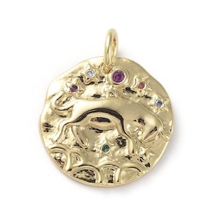May include: Gold-colored pendant featuring a detailed depiction of a bull, the Taurus zodiac symbol. The pendant is adorned with colorful gemstones and star-shaped accents. The pendant has a textured surface and a loop for attaching to a chain.