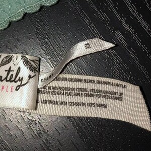 May include: A close-up of a tag from a piece of lingerie. The tag is white with the words "intimately FREE PEOPLE" in black script. The tag also has a size of 32A.