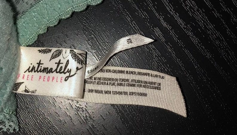 May include: A close-up of a tag from a piece of lingerie. The tag is white with the words "intimately FREE PEOPLE" in black script. The tag also has a size of 32A.