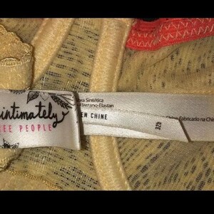 May include: Close-up of a beige bra with lace detailing. The bra features a tag with the words "intimately FREE PEOPLE" in black script. The tag also includes text in other languages. The bra is made in China.