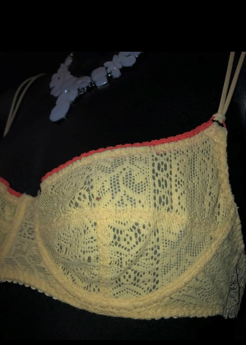 May include: A yellow lace bra with orange trim. The bra has adjustable straps and a delicate floral pattern. The bra is a lingerie item.