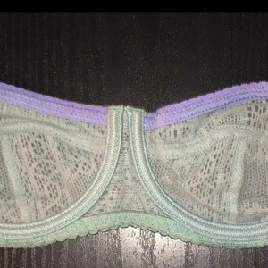 May include: A delicate, lacy bra in shades of pale green and lavender. The underwire bra features a scalloped edge and adjustable straps. The cups are made of a sheer, patterned fabric.