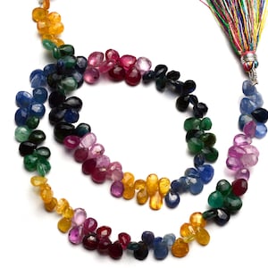 Puede incluir: Una hebra de cuentas de piedras preciosas en varios colores, incluyendo azul, verde, rojo, rosa y amarillo. Las cuentas son facetadas y tienen forma de lágrima. La hebra está enhebrada en un cordón con un borla al final.