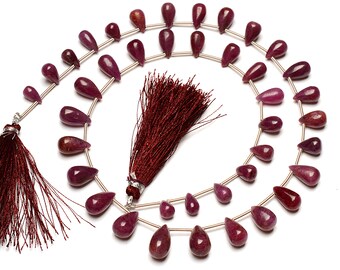 May include: A strand of ruby red gemstone beads in a teardrop shape. The beads are strung on a silver wire and are approximately 10mm in size. The strand is finished with a tassel on each end.