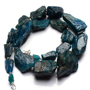 Puede incluir: Un collar hecho de piedras de apatita azul verdoso sin pulir con cuentas plateadas y un cierre plateado.