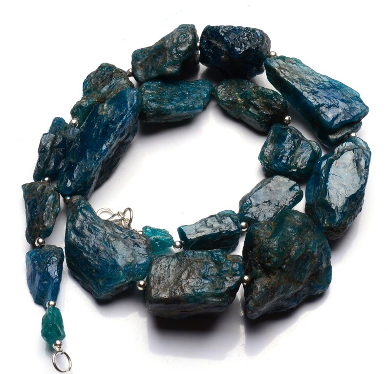 Puede incluir: Un collar hecho de piedras de apatita azul verdoso sin pulir con cuentas plateadas y un cierre plateado.