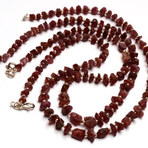 Può includere: Una lunga collana realizzata con piccole perle di rubino rosso irregolari infilate su una catena d'oro. La collana è a strati e ha due chiusure.