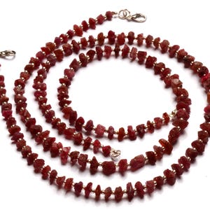 Könnte beinhalten: Eine lange Halskette aus kleinen, unregelmäßigen, roten Rubinperlen, die auf einem Silberdraht aufgefädelt sind.