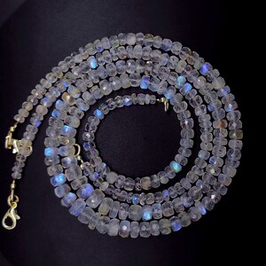 Op de afbeelding: Een lange streng van iriserende witte maansteen kralen, geregen op een zilveren ketting met een karabijn sluiting. De kralen zijn gefacetteerd en hebben een glinsterende, opalescente kwaliteit.