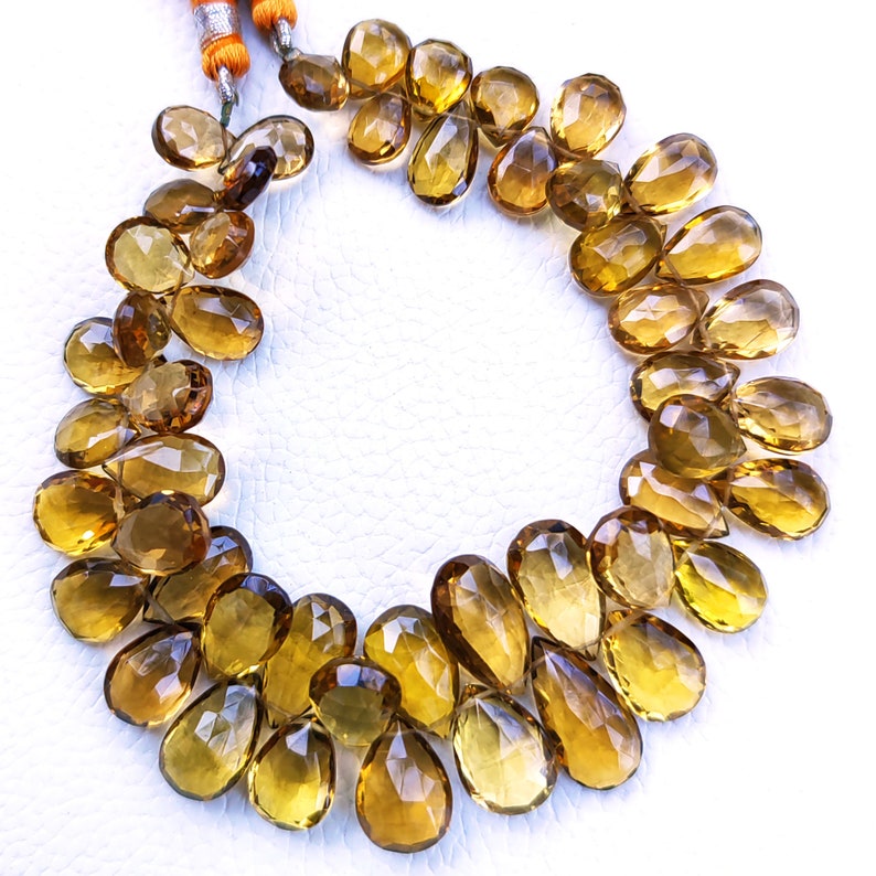 May include: A strand of golden brown gemstone beads, each bead is faceted and pear-shaped. The beads are strung together to form a necklace.