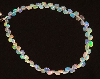 May include: A strand of white opal beads with iridescent rainbow colors. The beads are oval shaped and strung on a clear thread.