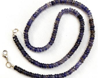 Könnte beinhalten: Eine Kette aus dunkelvioletten und grauen Edelsteinperlen mit silbernen Verschlüssen. Die Perlen sind facettiert und haben einen leicht schillernden Glanz.