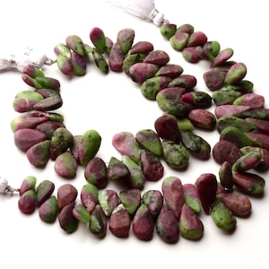 Op de afbeelding: Een streng groene en roze edelsteen kralen, met een druppelvorm. De kralen zijn geregen op een zilveren draad en hebben aan elk uiteinde een kwast.