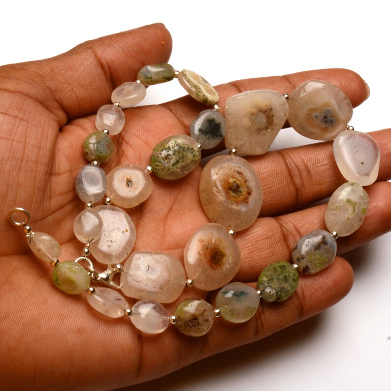 May include: A necklace featuring a variety of natural stone beads in shades of beige, green, and gray. The beads are strung together with silver-colored metal findings. The stones vary in size and shape, creating a unique and organic look.