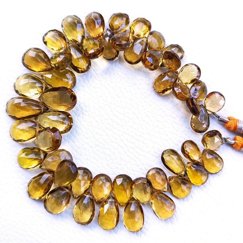 May include: A strand of golden brown teardrop-shaped gemstone beads. The beads are faceted and have a translucent appearance.