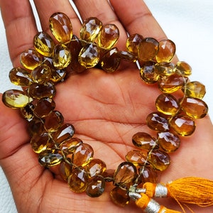 May include: A strand of faceted, golden brown gemstone beads, strung on a thin wire. The beads are oval-shaped and have a faceted, teardrop-like appearance. The strand is finished with two tassels.